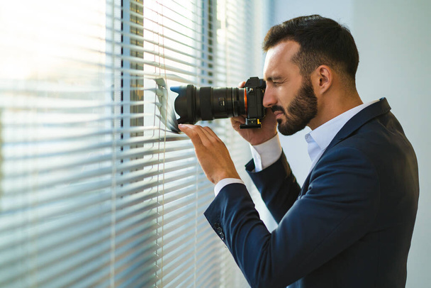 El hombre con una cámara fotografiando a través de las persianas
 - Foto, Imagen