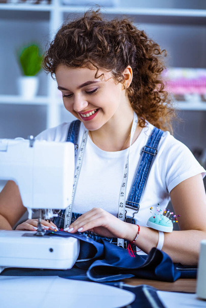 La mujer feliz trabajando cerca de la máquina de coser
 - Foto, imagen
