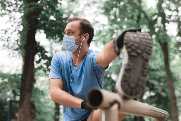 Sportman met medisch masker en handschoenen, smartphone en oordopjes aan het trainen, joggen in de stedelijke omgeving. - Foto, afbeelding