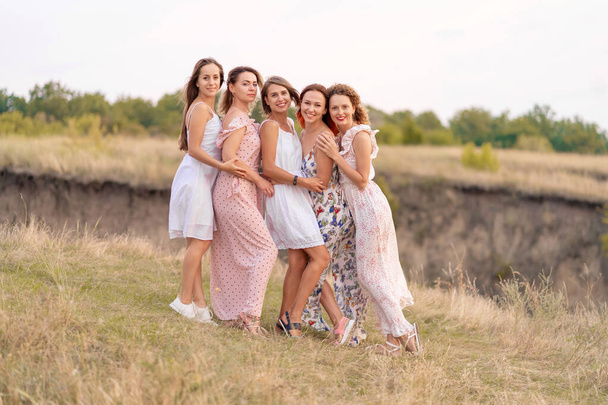 A cheerful company of beautiful girls friends enjoy the company and have fun together in a picturesque place of green hills - Zdjęcie, obraz