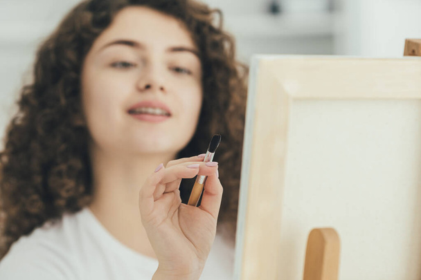 Roztomilý kudrnatý malíř maluje obrázek na stojan - Fotografie, Obrázek