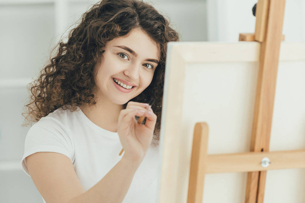 A menina encaracolado bonito pintando um quadro no cavalete
 - Foto, Imagem