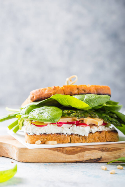 Veganes Sandwich mit Tofu, Spinat, Rettich, Spargel und grünem Dressing auf dem Brett. - Foto, Bild