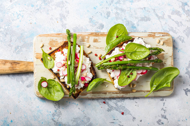 Vegan sandwich met tofu, spinazie, radijs, asperges, en groene dressing op het bord. - Foto, afbeelding