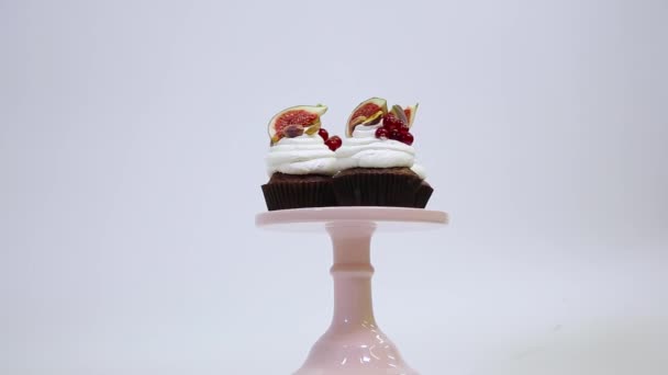 Three delicious chocolate cupcakes decorated with white cream cheese, figs, red currant, pistachios on the spinning dessert stand. White background. - Filmati, video