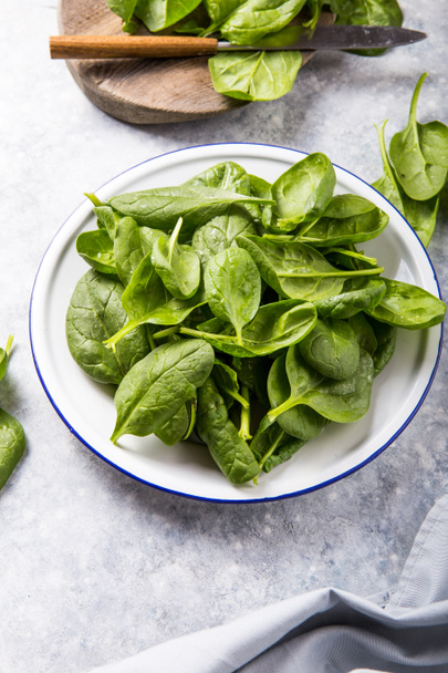 Baby spinach leaves in bowl on grey concrete background, top view, copy space. Clean eating, detox, diet food ingredient - Фото, зображення