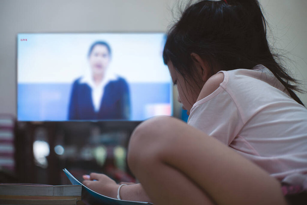 Μικρό κορίτσι μαθαίνοντας DLTV ή εξ αποστάσεως εκπαίδευση Τηλεόραση στο φορητό υπολογιστή στο σπίτι, Κοινωνική απόσταση κατά τη διάρκεια της καραντίνας, Online έννοια της εκπαίδευσης - Φωτογραφία, εικόνα