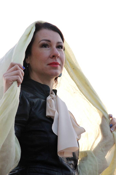 vrouw met rode lippenstift bij zonsondergang. Europese vrouw in een zwarte jas, beige blouse en met een sjaal op het hoofd. - Foto, afbeelding