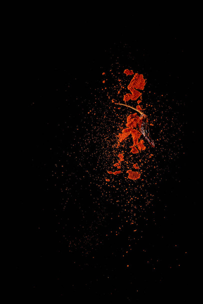 Red paprika spices powder explosion, flying chili pepper isolated on black background. Splash of spice background.  - Фото, изображение