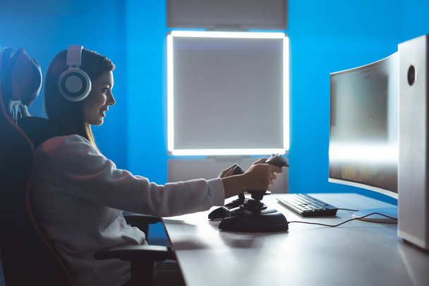 A garota gamer com fones de ouvido jogando jogos de vídeo no quarto escuro
 - Foto, Imagem