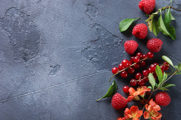 Fresh berries: raspberries and red currants. Red flowers on a branch, green leaves on a dark grey background. Sakura. Flatlay, top view. Background image, copy space  - Foto, Imagem