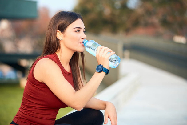 Thirsty young sporty woman making pause and drinking water during exerising. - Фото, изображение