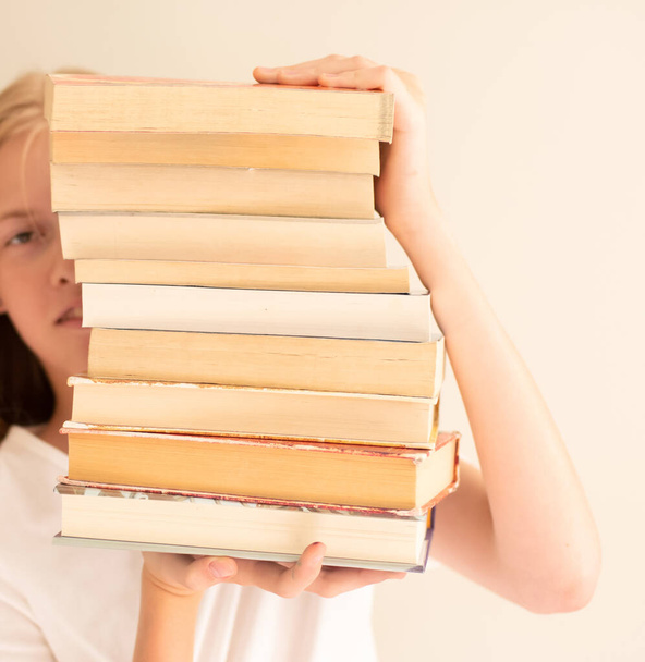 Ένα έφηβο κορίτσι που κρύβεται πίσω από ένα σωρό βιβλία. Φοιτητική ζωή και επιστροφή στο σχολείο - Φωτογραφία, εικόνα