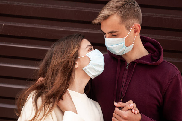 Young loving couple wearing face masks, hugging and looking at each other eyes outdoor - 写真・画像