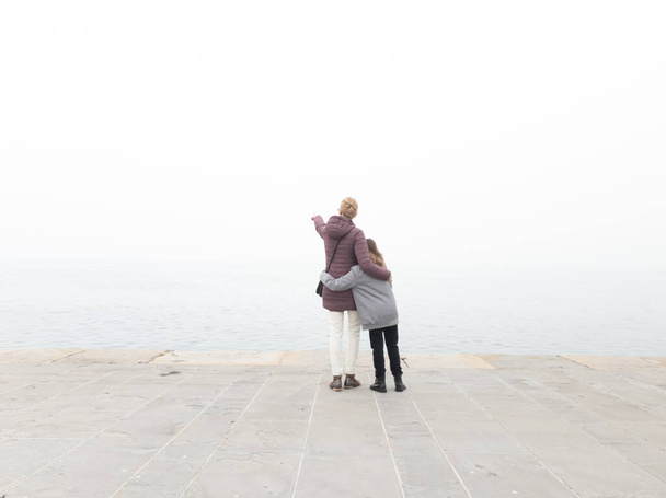 Matka i dziewczyna dziecko na wybrzeżu morza patrząc na daleki mglisty horyzont. - Zdjęcie, obraz