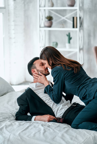 The happy man and woman in suits kissing in the bed - 写真・画像