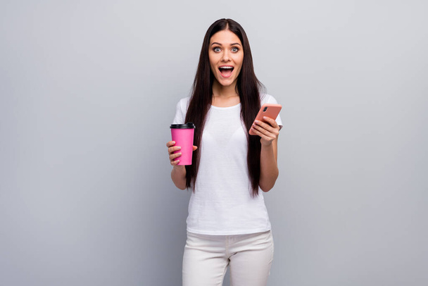 Portrait of her she nice attractive lovely lovable amazed cheerful straight-haired girl holding in hands using cell drinking latte having fun isolated over light gray pastel color background - Foto, Imagen