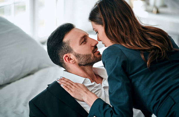 Ο άντρας και η γυναίκα με τα κοστούμια φιλιούνται στο κρεβάτι. - Φωτογραφία, εικόνα