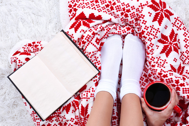 Composition with warm plaid, book, cup of hot drink and female legs, on color carpet background - Foto, imagen