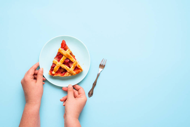 Slice of rhubarb pie on a plate, on a blue background. Flat lay of a woman serving a portion of  English rhubarb cake. Eating a piece of the pie. - Foto, Bild