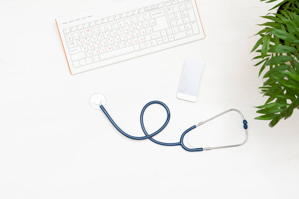 Keyboard, phone and stethoscope on a wooden background. The view from the top. Doctor's workplace - 写真・画像