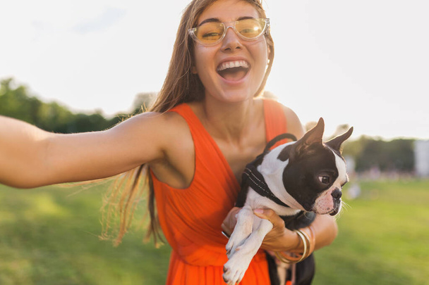 young happy smiling woman in orange dress having fun playing with dog in park, summer style, cheerful mood, making selfie photo on camera - Foto, Imagem