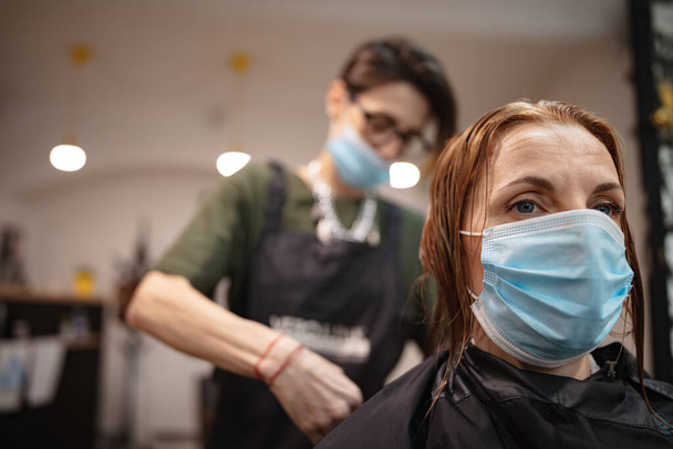 Virüs salgını sırasında salonda maskeli bir kuaför ve müşteri. Güvenlik maskesi ile çalışmak. - Fotoğraf, Görsel