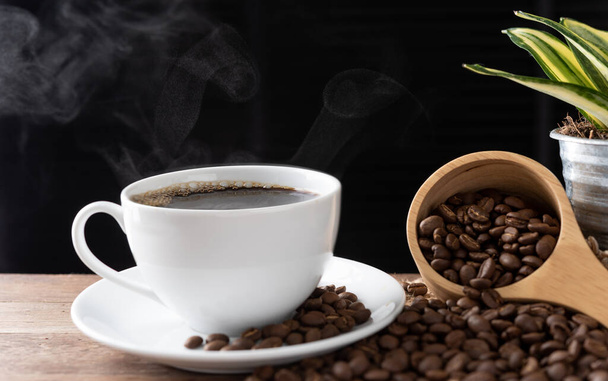 Steam coffee cup with roasted beans and flower pot on wood background in morning sunlight - Photo, Image