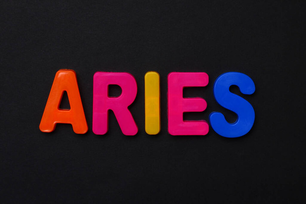 Aries text. Zodiac sign written in bright multi-colored cheerful letters on a black dramatic background. Low dark key. Horoscope Theme - Photo, Image