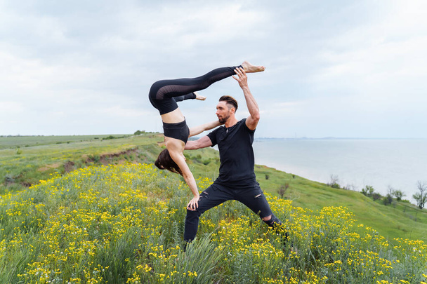 Coppia praticare acro yoga pone all'aperto. Coppia di acrobati sportivi che mostrano un allenamento di classe di flessibilità. L'atleta che tiene in braccio la ragazza, che fa a testa in giu '. Donna che tiene il suo corpo con i muscoli
 - Foto, immagini