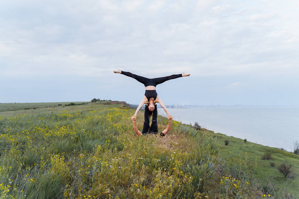 Due giovani sportivi che fanno esercizio fitness acro yoga insieme all'aperto. Elementi acrobatici per forza ed equilibrio in mare in collina. Uomo sollevamento e bilanciamento donna. Stile di vita sano
 - Foto, immagini