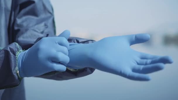 Close-up of human hand putting on blue protective glove. Unrecognizable worker in antiviral suit getting ready to disinfect public place outdoors. Covid-19, air pollution, global hazard. - Materiaali, video