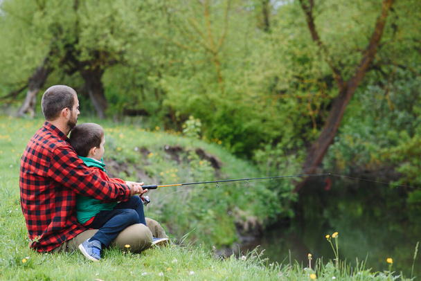 A father teaching his son how to fish on a river outside in summer sunshine - Foto, immagini