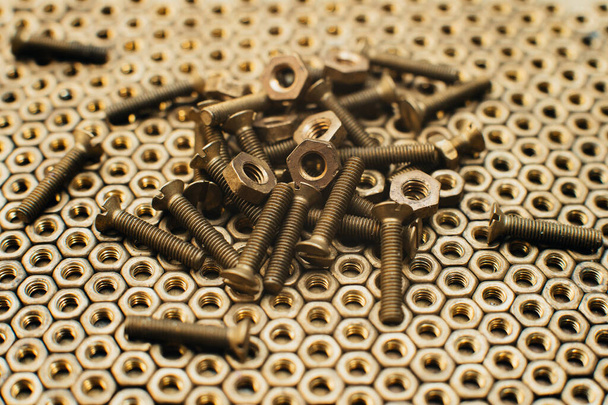 Close-up, macro. Old Soviet brass countersunk head screws with a flat head screwdriver. Texture, background of brass nuts laid out in the form of honeycombs. Gold color screws. Dirty wood screws in oi - Photo, Image