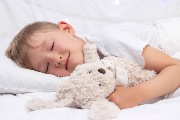 Charming little white boy sleeps in bed. hugs a soft toy - Foto, Bild