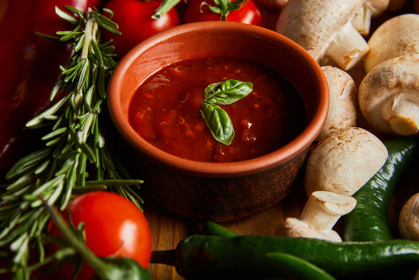 селективний фокус томатного соусу з листям базиліка біля помідорів вишні, зеленого перцю чилі, грибів та розмарину
  - Фото, зображення