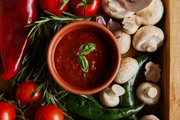 top view of tomato sauce with basil leaves near cherry tomatoes, green chili peppers, mushrooms and rosemary  - Фото, изображение