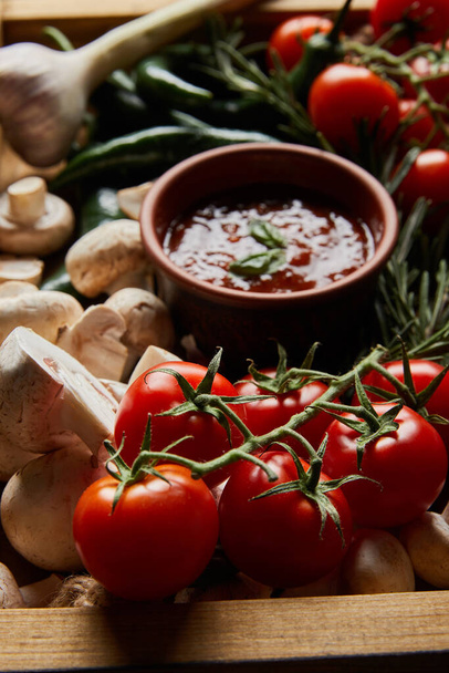 selective focus of mushrooms, cherry tomatoes, tomato sauce near rosemary and green chili peppers in wooden box  - Valokuva, kuva