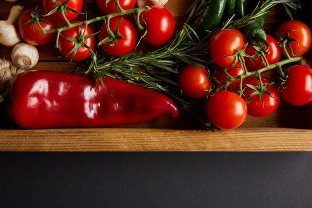 top view of cherry tomatoes, mushrooms near rosemary and red chili pepper in wooden box on black - 写真・画像