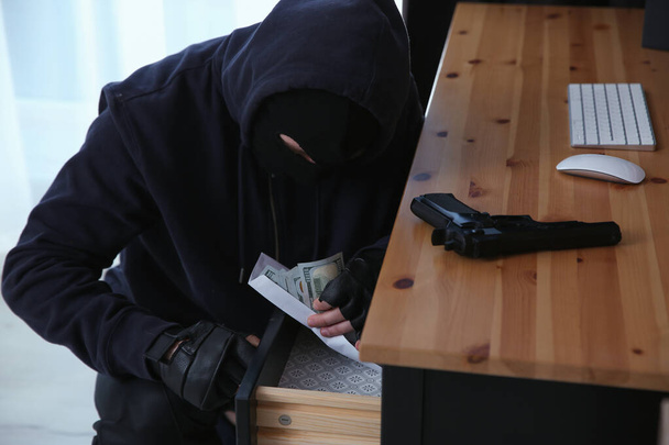 Dangerous masked criminal stealing money from house - Фото, изображение