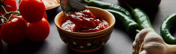 panoramisch concept van lepel in smakelijke tomatensaus bij rijpe groenten op zwart - Foto, afbeelding
