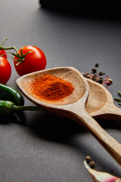 selective focus of organic cherry tomatoes, peppercorns, wooden spoons with paprika powder and green chili peppers on black - Фото, зображення