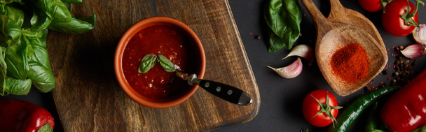horizontal crop of red cherry tomatoes, tomato sauce, peppercorns, herbs and green chili peppers near cutting board on black - Fotoğraf, Görsel