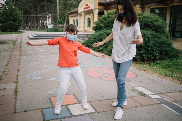 Young woman and cute girl at playground markings using protection masks - Valokuva, kuva