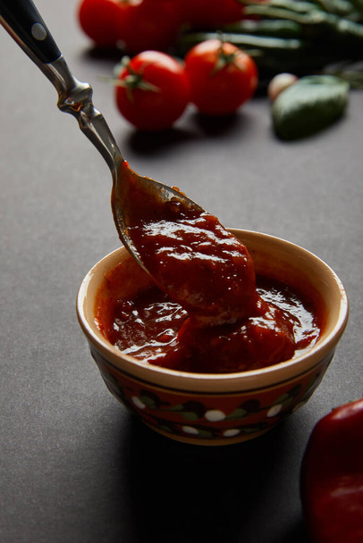 selective focus of spoon in bowl with tomato sauce on black  - 写真・画像