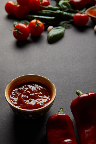 vista superior del tazón con salsa de tomate cerca de chiles picantes en negro
  - Foto, Imagen