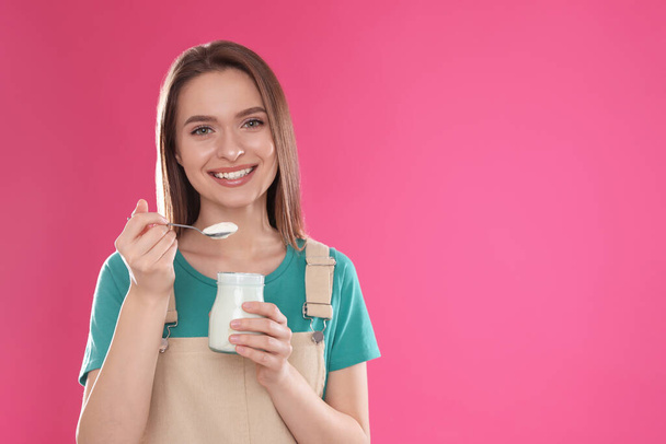 Nuori viehättävä nainen, jolla on maukas jogurtti vaaleanpunaisella taustalla. Tekstitila
 - Valokuva, kuva