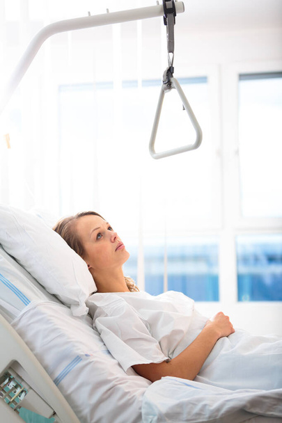 Pretty, young, female patient in a modern hospital room. Getting better fast after a surgery - pensive yet positive, thinking ahead, making plans (shallow DOF; color toned image) - Foto, Imagem