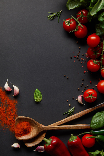 top view of cherry tomatoes, spicy chili peppers, garlic cloves and fresh herbs near spoons with paprika powder on black  - Foto, imagen