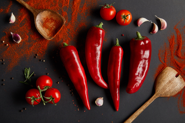 vista superior de chiles picantes, tomates cherry y romero fresco cerca de cucharas con pimentón en polvo sobre negro
  - Foto, imagen